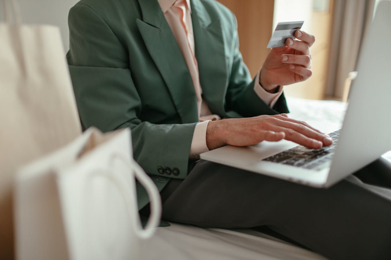 Close-up of a man in a teal blazer shopping online using a laptop and credit card, indoors.