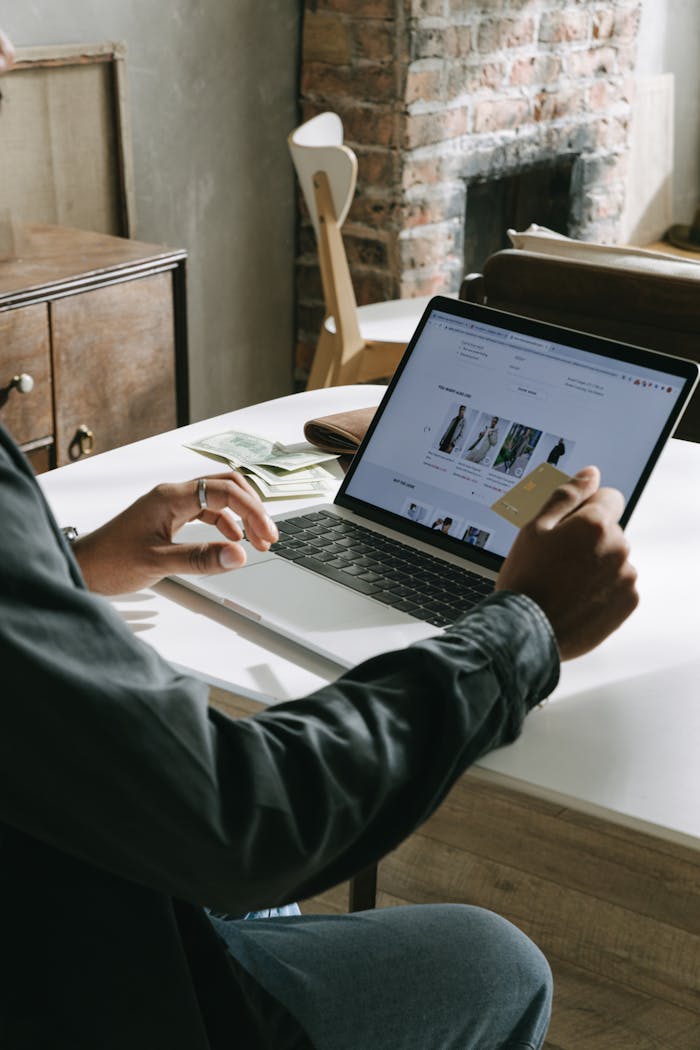 An adult uses a credit card for online shopping on a laptop indoors.